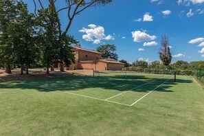 Una cancha de tenis con una red, rodeada de árboles y un edificio al fondo.