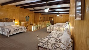 A room with two beds, wooden walls, a ceiling fan, and a small staircase.