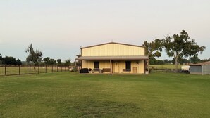 A large, single-story barn with a covered porch and a fenced-in grassy area in front.