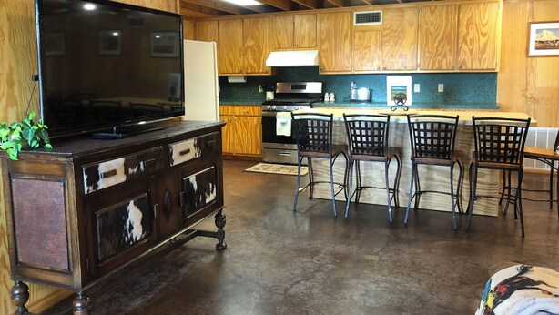 A wooden interior with a TV on a cabinet, a kitchen area with a microwave, and a dining space with chairs.