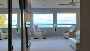 A spacious living room with large windows, a ceiling fan, and a view of the ocean. - Relaxing in an Entire 5,400sf Beach View Home With Indoor Heated Swimming Pool. (Federal Way)