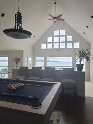 A spacious room with a pool table, comfortable seating, large windows with a view, and a ceiling fan. - Relaxing in an Entire 5,400sf Beach View Home With Indoor Heated Swimming Pool. (Federal Way)