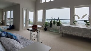 A spacious living room with a large window, a sofa, a coffee table, and a laptop on a cart. - Relaxing in an Entire 5,400sf Beach View Home With Indoor Heated Swimming Pool. (Federal Way)
