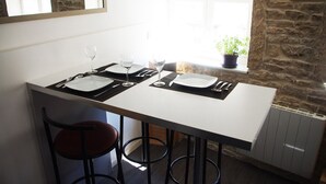 A dining area with a white table set for two, two black barstools, and a stone wall in the background. - Wood Stone & Wine **** (Beaune)