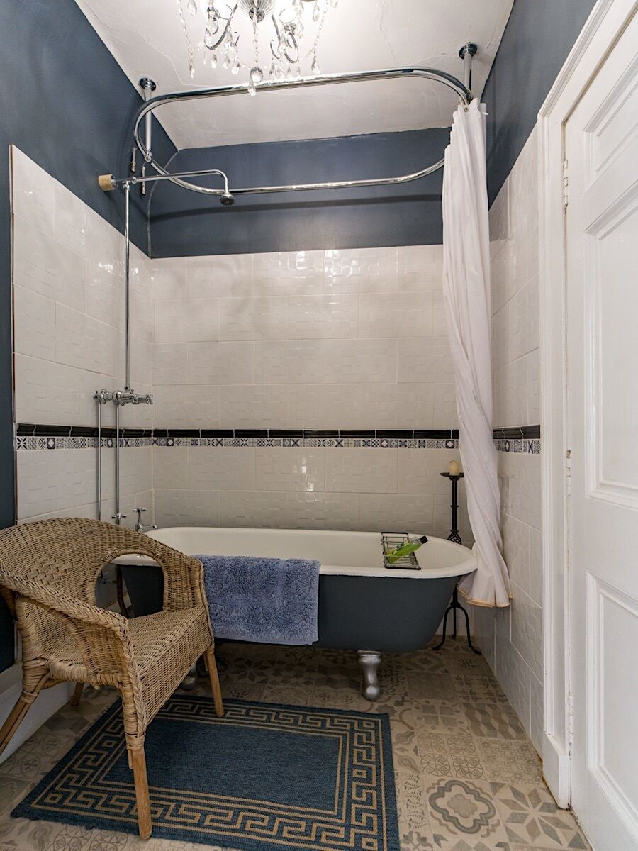 Un baño con bañera, ducha, una silla de mimbre y un tapete estampado.