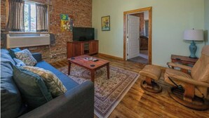 Een woonkamer met een bakstenen muur, een bank, een salontafel, een stoel en een deur die leidt naar een andere kamer.