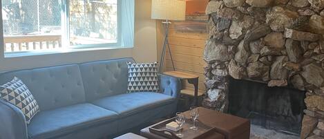 A cozy living room with a stone fireplace, a blue sofa, and two brown ottomans.