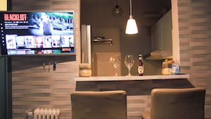 Un coin bar avec un téléviseur diffusant une émission, deux tabourets de bar, un verre à vin et une bouteille.