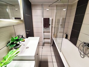A modern bathroom with a white sink, a mirror, a potted plant, and a shower area.