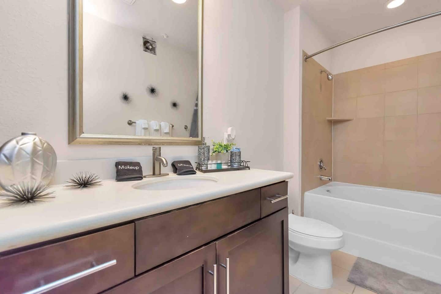 A modern bathroom with a white sink, dark wooden vanity, a large mirror, and a white toilet.