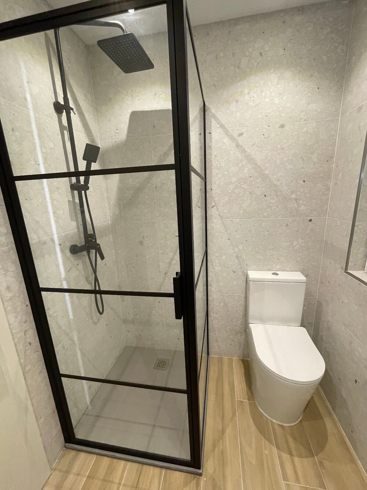 A glass-enclosed shower with a handheld showerhead and a wall-mounted faucet.