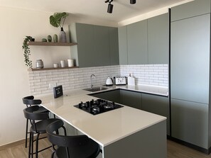 A modern kitchen with a central island, bar stools, a built-in oven, and a refrigerator.