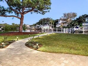 A waterfront property with a paved walkway, a large tree, and a dock with boats.