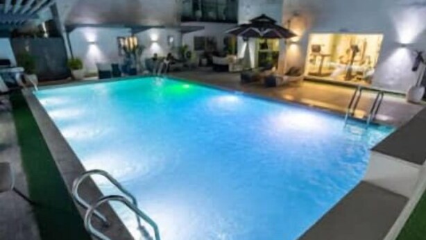 An indoor swimming pool with a clear blue water, a poolside lounge area, and a well-lit environment. - Zen Apartments (Lagos)