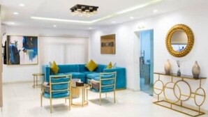 A modern living room with a blue sectional sofa, a coffee table, and a gold-framed console table with vases. - Zen Apartments (Lagos)