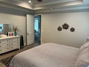 A bedroom with a large bed, a dresser with drawers, a mirror, and a door leading to a hallway.