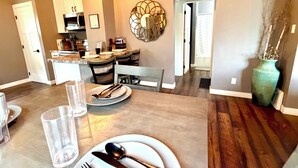 A dining area with a table set for four, a kitchen in the background, and a decorative wall piece. - Cozy, 2-bedroom vacation home. 1 mile to DT: Hot Tub, 86" TV, Golf & Fenced Yard (Sioux Falls)