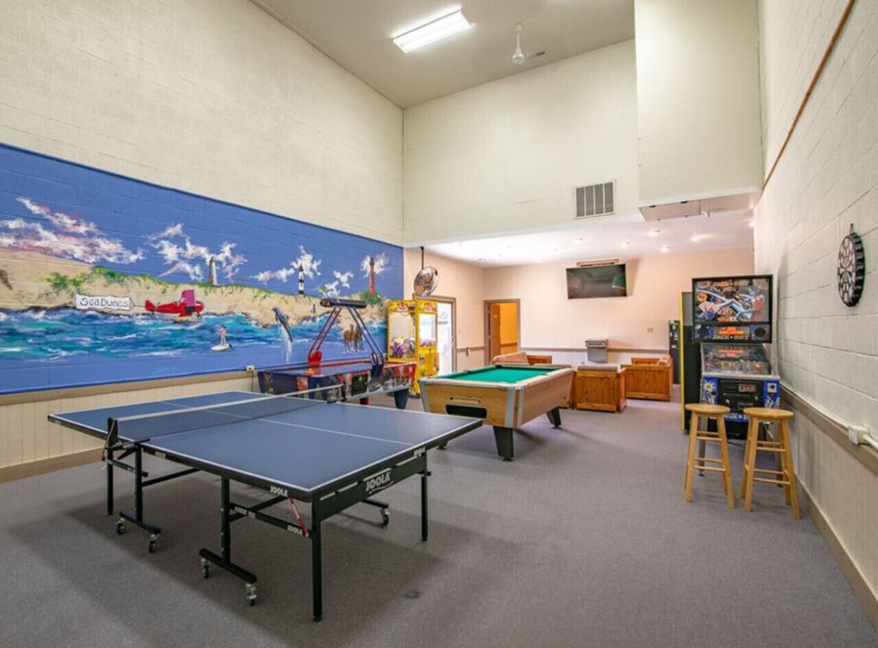 A room with a ping pong table, a pool table, and a mural of a beach scene.