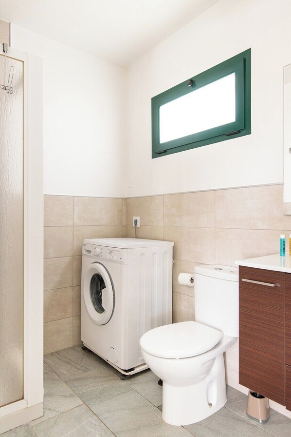 A compact bathroom with a washing machine, toilet, and a small cabinet with toiletries.