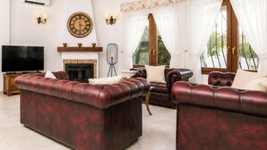 Un salon avec une cheminée, des canapés en cuir, un téléviseur et une horloge au mur.