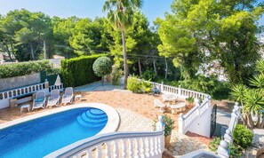 A swimming pool with lounge chairs, surrounded by a white fence and lush greenery.