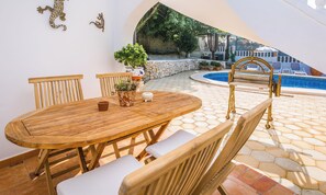 An outdoor patio with a wooden table and chairs, a pool, and a stone wall.