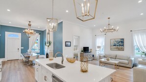 A modern kitchen with a central island, white cabinetry, and stainless steel appliances. There are pendant lights above the island and a dining area with a table and chairs. - Luxury 5BR Home, Walk to French Quarter!! (New Orleans)