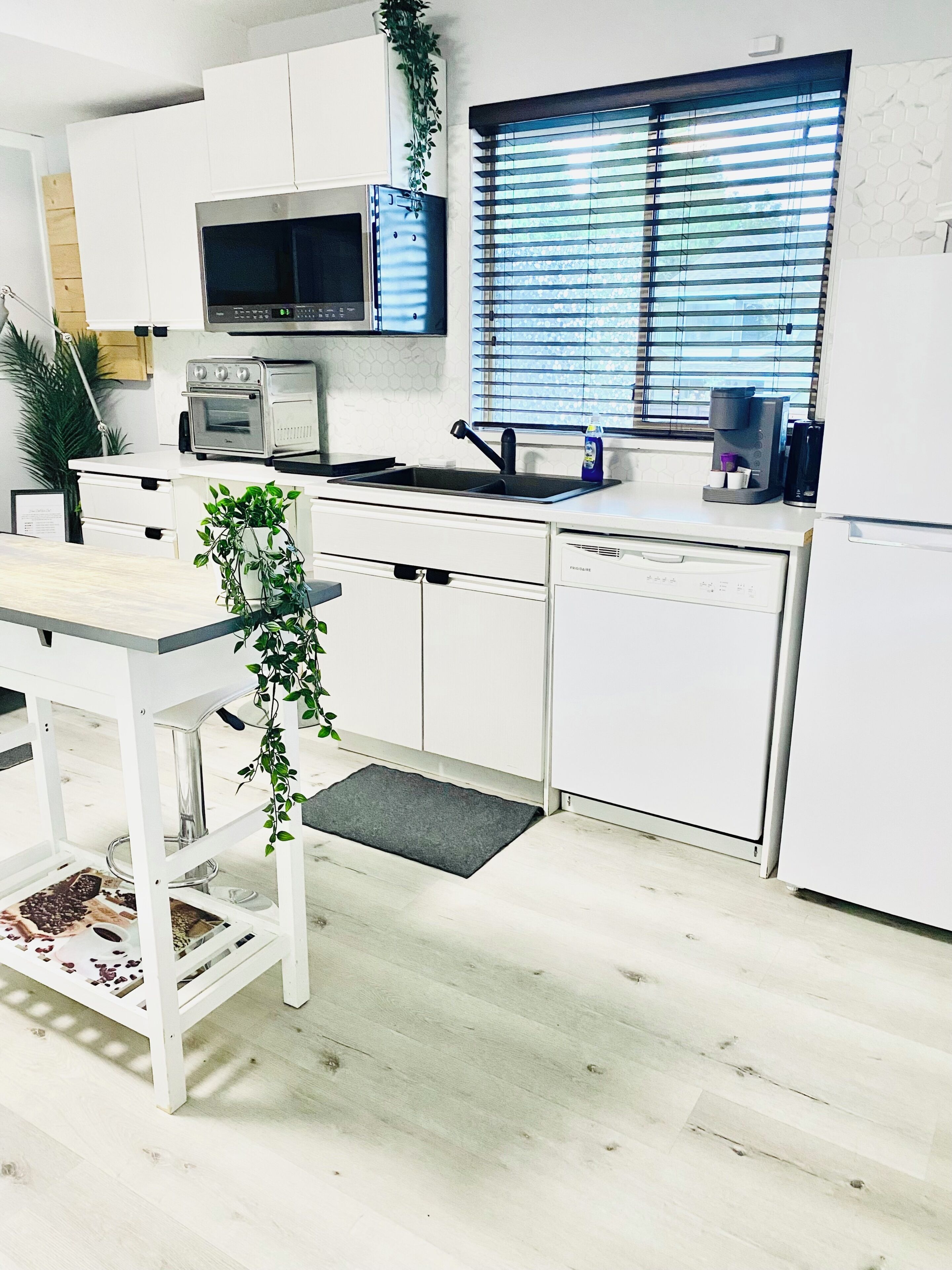 A modern kitchen with white cabinetry, a built-in microwave, a coffee maker, and a window with blinds.