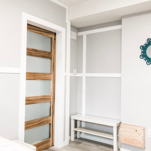 Una habitación con un armario de madera, estanterías blancas y un pequeño escritorio de madera.