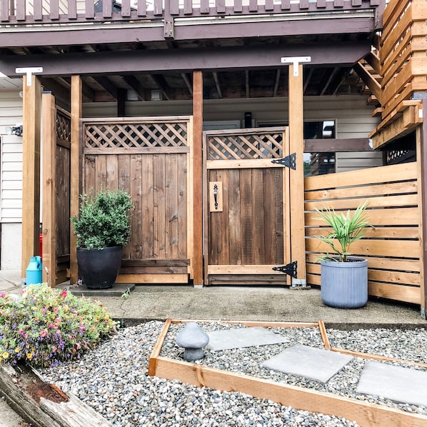 Una verja de madera con diseño de celosía, una planta en maceta y un pequeño jardín con grava y piedras para pisar.