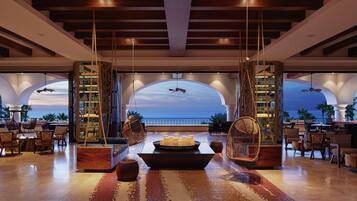 A spacious lobby with a large seating area, a central decorative table, and a view of the ocean through arched windows.
