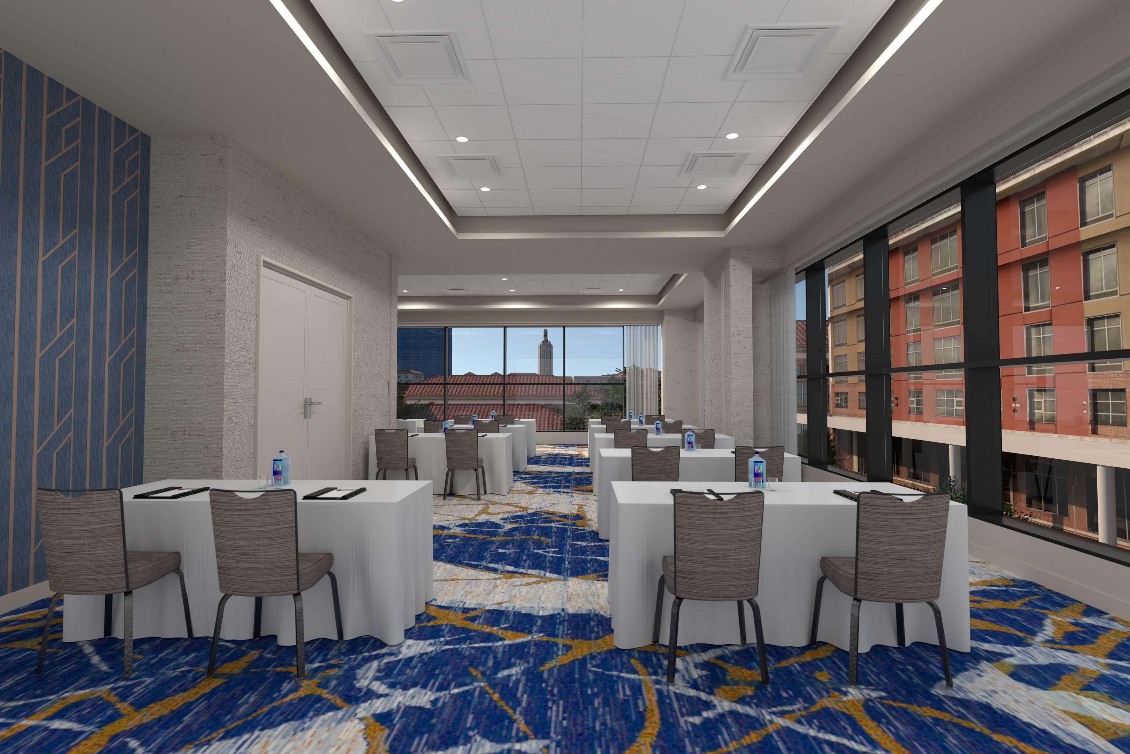 A conference room with tables and chairs, a patterned carpet, and a view of buildings through large windows.