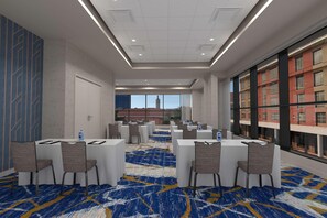 A conference room with tables and chairs, a patterned carpet, and a view of buildings through large windows. - Hilton Grand Vacations Club La Pacifica Los Cabos (San José del Cabo)