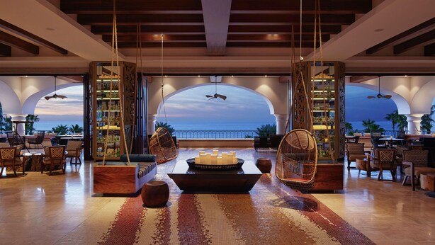 A spacious lobby with a large seating area, a central decorative table, and a view of the ocean through arched windows. - Hilton Grand Vacations Club La Pacifica Los Cabos (San José del Cabo)