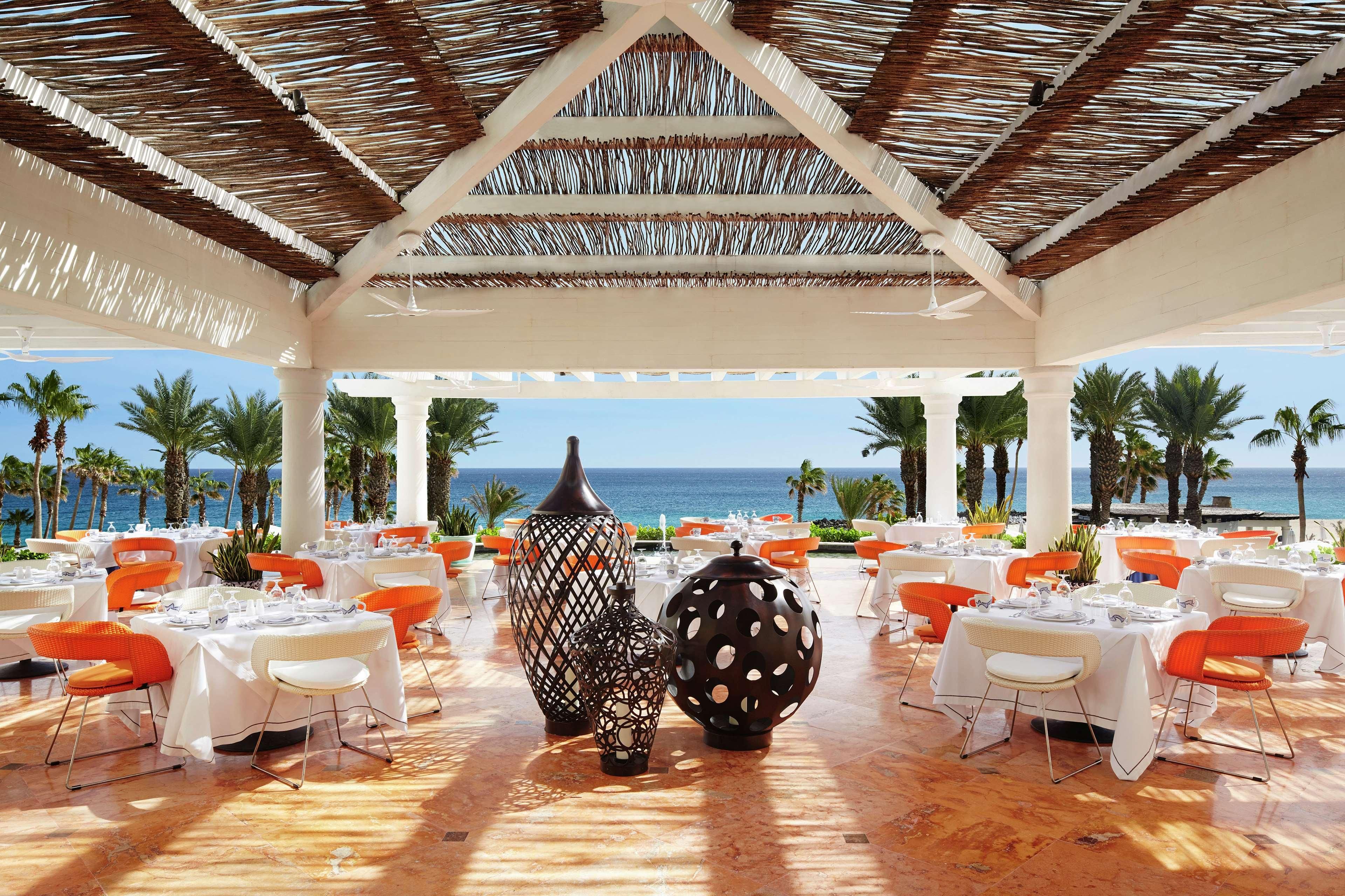An outdoor dining area with tables and chairs, large decorative vases, and a view of the ocean.