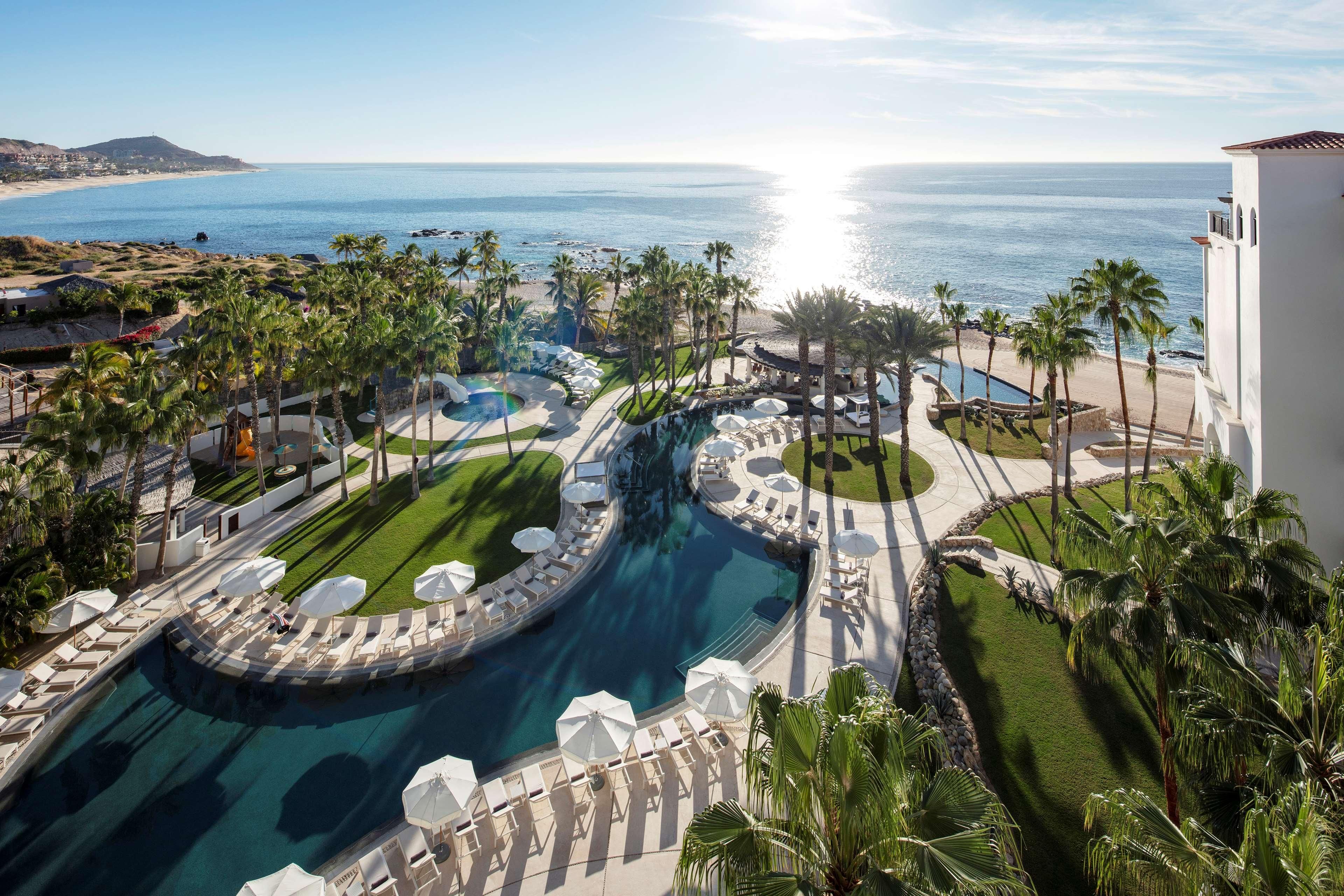 Un resort con piscina, palme e vista sull'oceano.