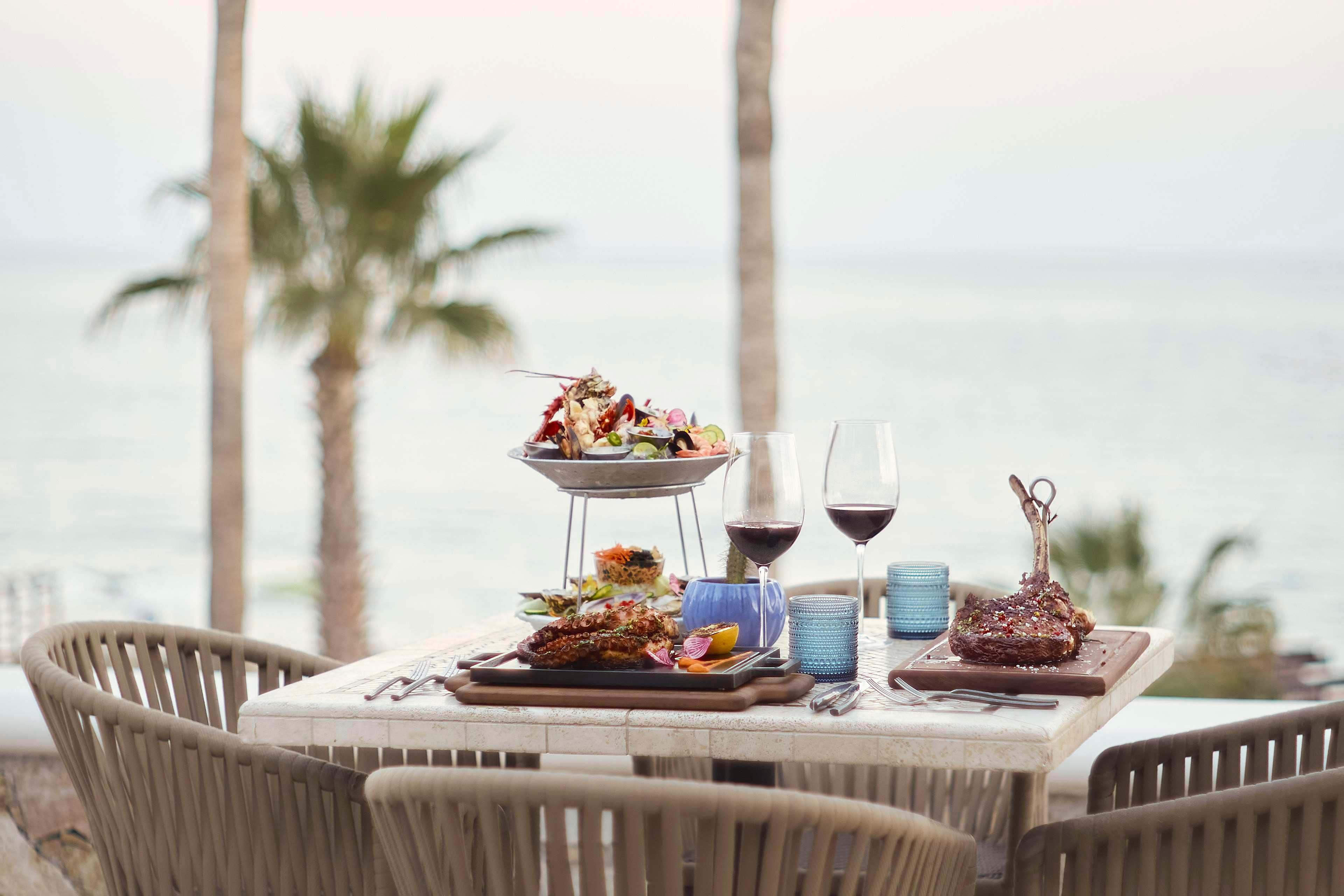 Una mesa con comida y bebidas, sillas al aire libre y vistas al océano.