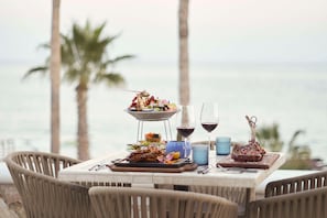 A dining table with food and drinks, outdoor chairs, and a view of the ocean.
