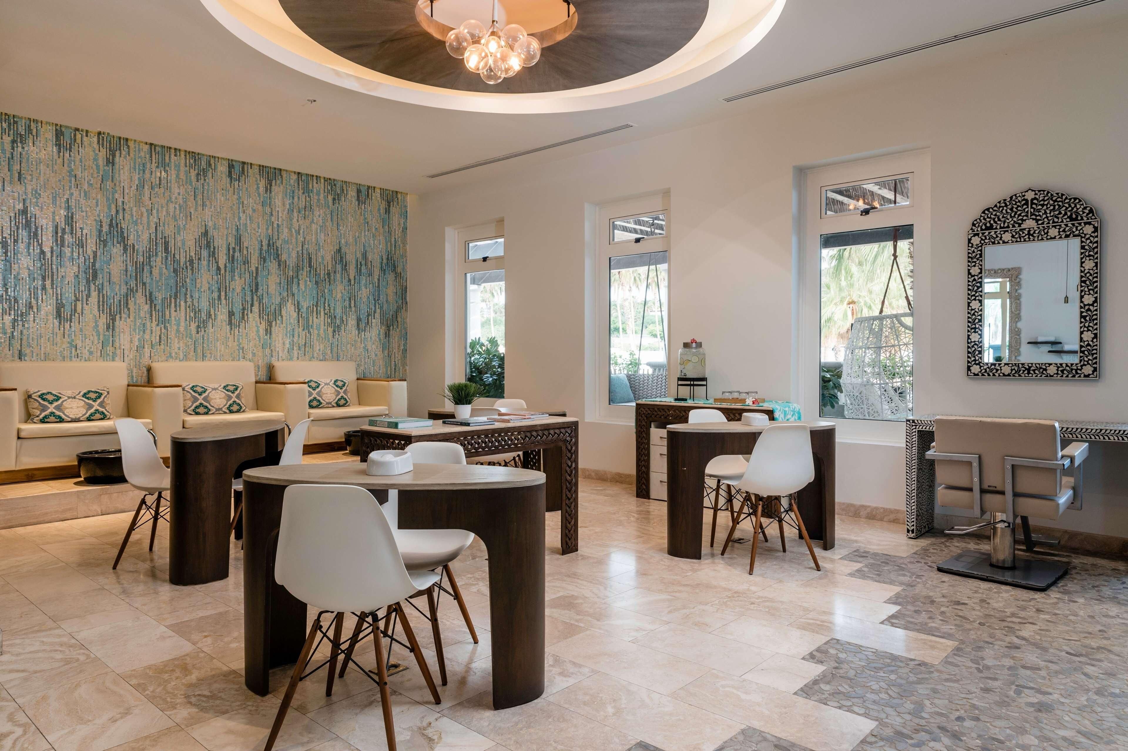 A modern interior with a sofa set, dining tables, chairs, a chandelier, and a large abstract wall painting.