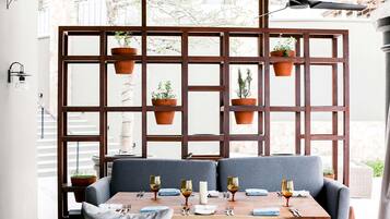 A dining area with a table set for four, a wooden partition with hanging planters, and a ceiling fan.