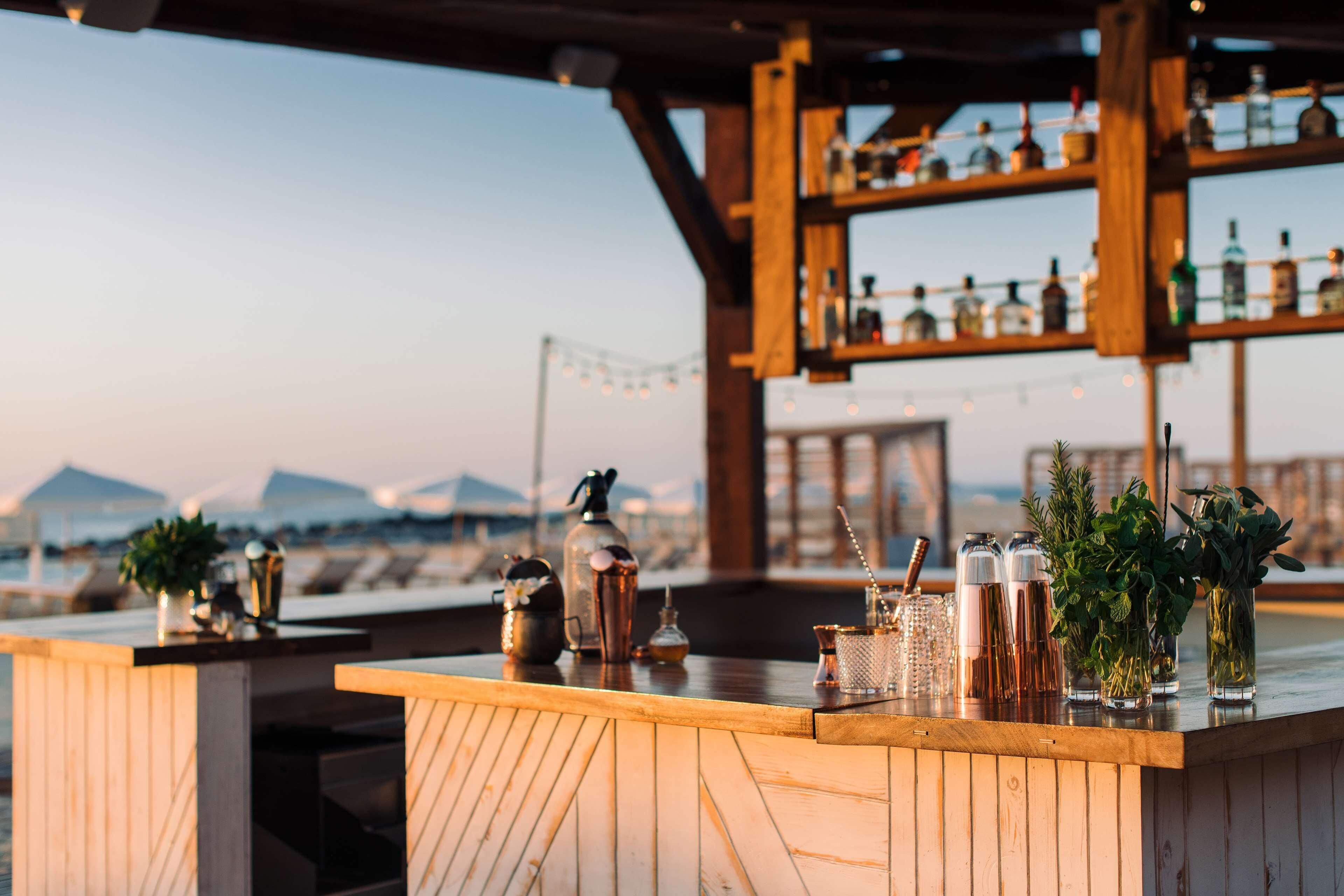 A bar with wooden shelves and various bottles, a wooden counter, and a view of the mountains in the background.
