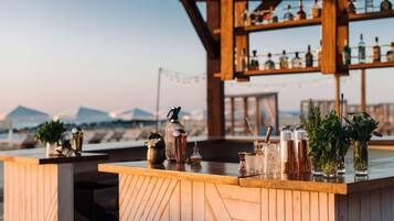 A bar with wooden shelves and various bottles, a wooden counter, and a view of the mountains in the background.