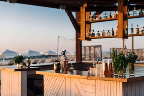 Un bar con estanterías de madera y varias botellas, una barra de madera, y vistas de las montañas al fondo.