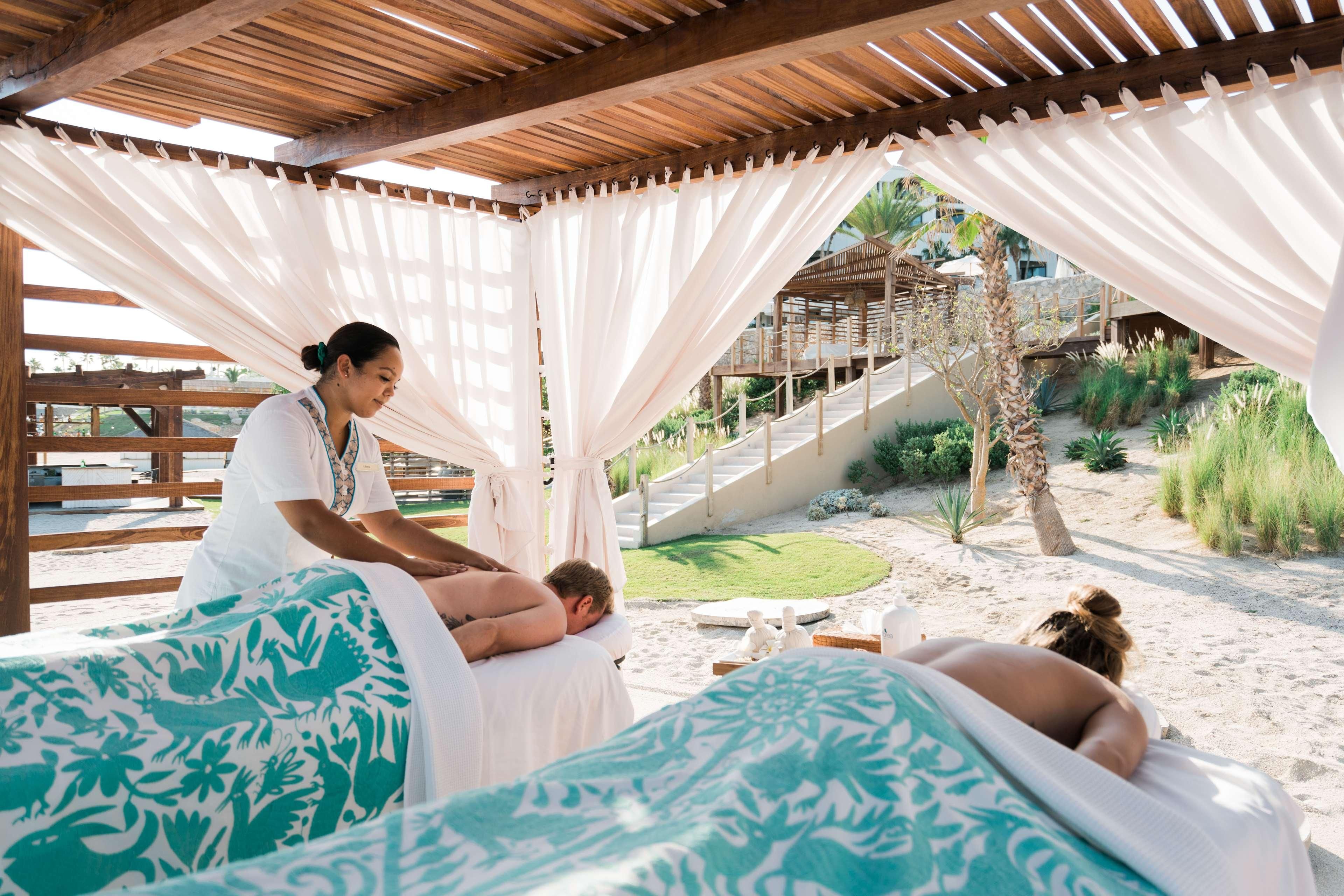 A spa area with massage tables, a wooden pergola, and a view of a landscaped garden and pool.