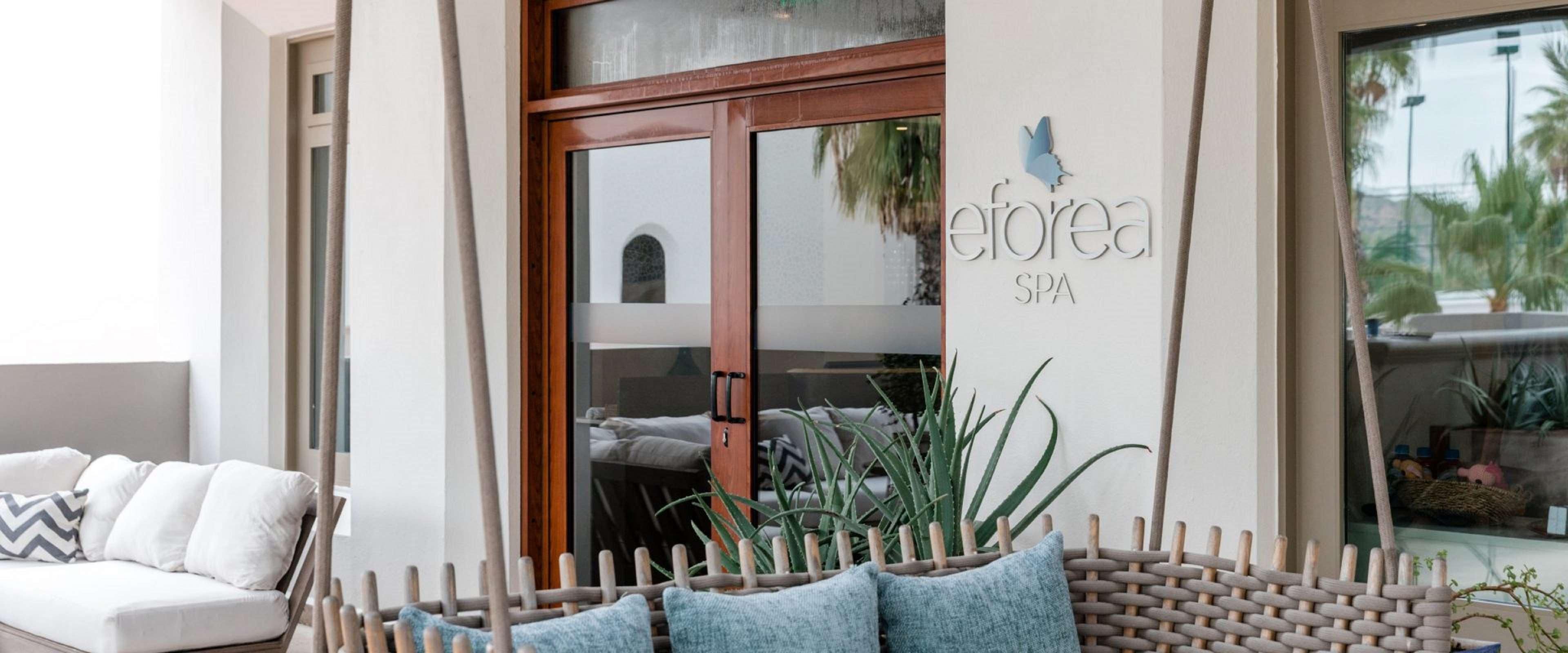 A spa entrance with a wooden door, a sign reading 'eforea SPA,' and a wicker bench with cushions.