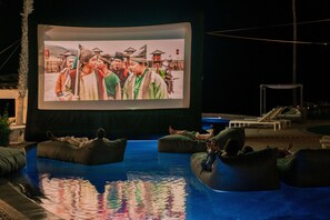 A large outdoor screen displaying a movie, surrounded by bean bags and a swimming pool. - Hilton Grand Vacations Club La Pacifica Los Cabos (San José del Cabo)