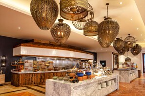 A well-lit buffet area with a marble counter, various food items, and hanging ornate light fixtures. - Hilton Grand Vacations Club La Pacifica Los Cabos (San José del Cabo)