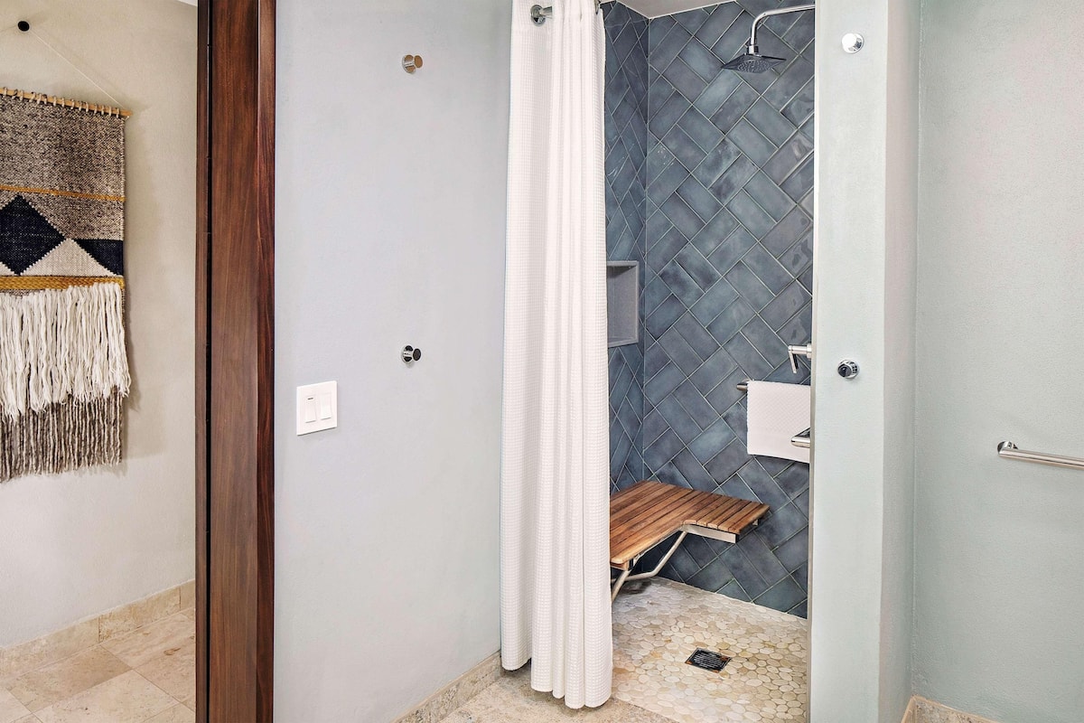 Une salle de bain avec une douche, un banc en bois, un porte-serviettes et un mur décoré d’un motif.