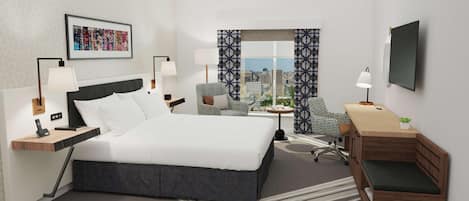 Habitación de hotel con cama, dos sillas, un escritorio, televisión y vista a la ciudad.