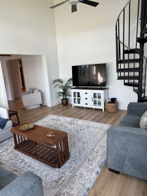 Una sala de estar moderna con un televisor de pantalla plana, una mesa de centro de madera, sofás grises, un tapete estampado y una escalera.